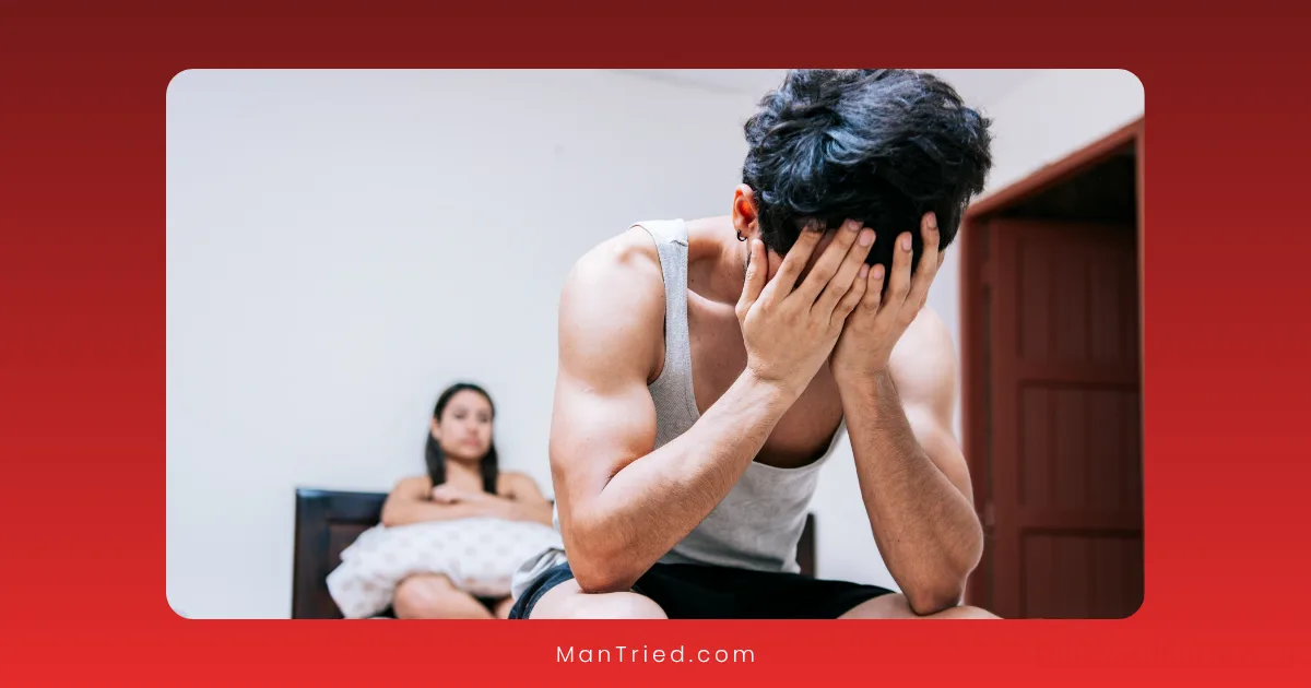 A man sits on the edge of a bed with his head in his hands, appearing upset—possibly due to ED in younger men. In the background, a woman holds a pillow, watching him. The atmosphere suggests tension or sadness.