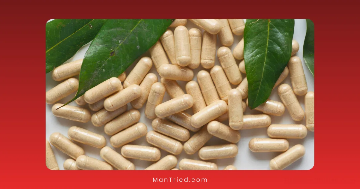 A pile of beige capsules scattered on a surface with two large green leaves on top, set against a red background—suggesting ashwagandha for testosterone.