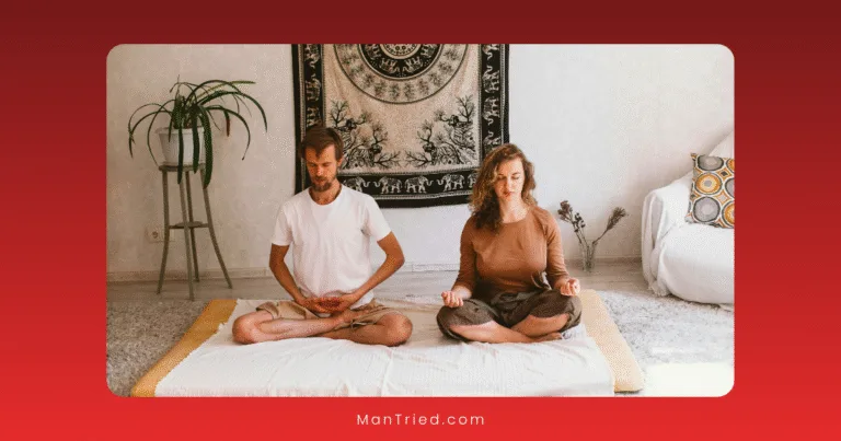 A man and woman sit cross-legged on a mat indoors, meditating with eyes closed. A decorative wall hanging and a plant are in the background. The calm space suggests they might be practicing breathwork for performance anxiety.