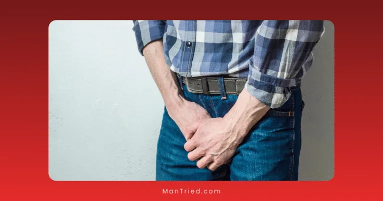 A person wearing a plaid shirt and jeans stands against a wall, holding their hands over their groin area as if in discomfort or pain, perhaps reflecting anxiety over chronic vs situational premature ejaculation.