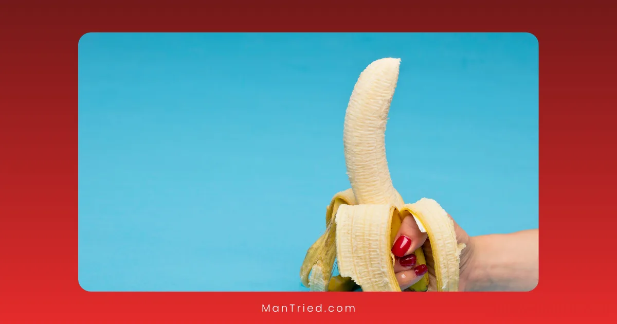 A hand with red painted nails holds a partially peeled banana upright against a blue background, subtly illustrating the early signs of Peyronie's disease.
