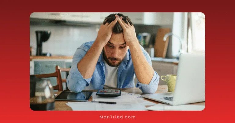A man sits at a kitchen table, showing signs of financial stress as he stares anxiously at papers, a calculator, and a laptop. His worry is evident—highlighting how financial concerns can impact overall health, including sexual health.