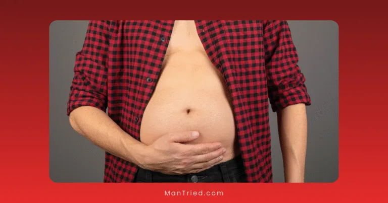 A person wearing a red and black plaid shirt, unbuttoned to reveal a bare, bloated stomach, holds their abdomen with one hand—highlighting the connection between gut health and sexual function against a plain background.