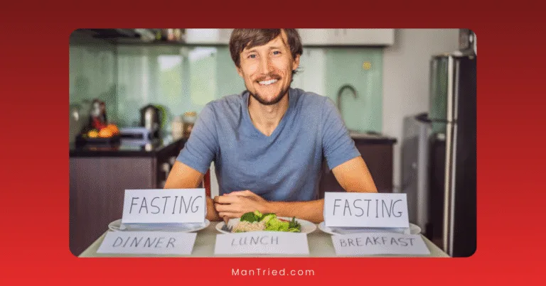 A man smiles while sitting at a table with a plate of food and three signs labeled FASTING DINNER, LUNCH, and FASTING BREAKFAST in a modern kitchen, highlighting his commitment to intermittent fasting for better health and sexual health.