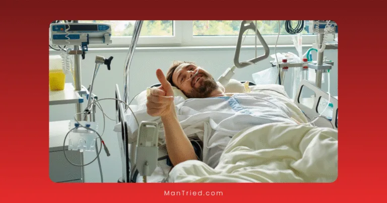 A man lies in a hospital bed, smiling and giving a thumbs-up during his penile surgery recovery, surrounded by medical equipment. Sunlight streams through a window in the background.