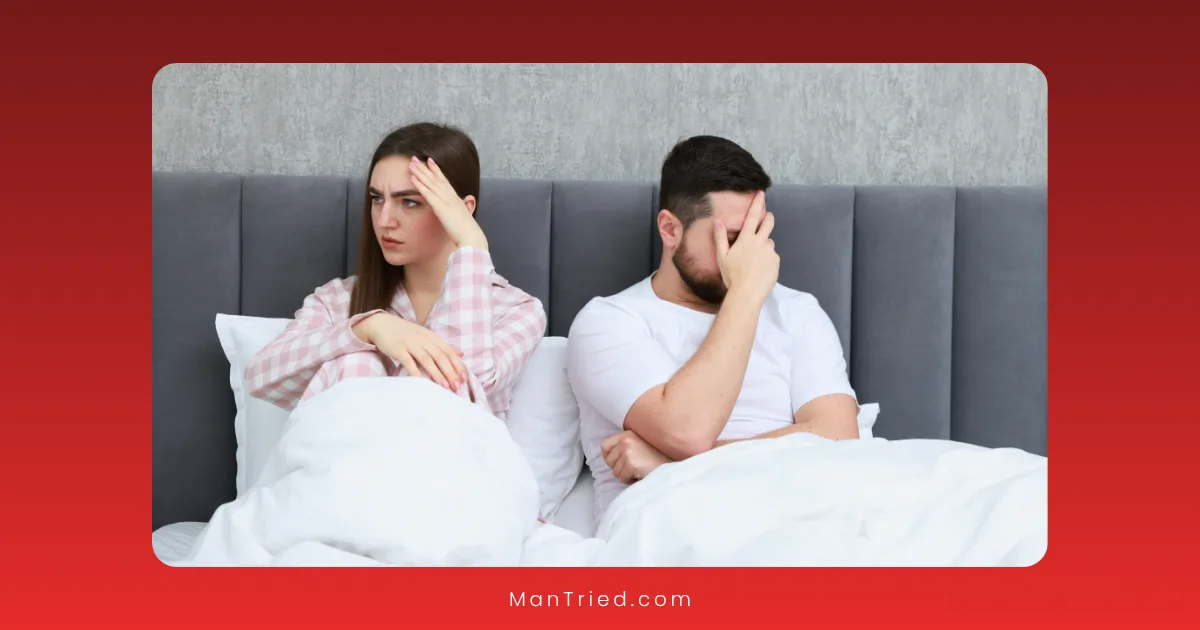 A woman and a man sit in bed, both looking upset and avoiding eye contact, perhaps strained by the psychological causes of delayed ejaculation. The woman has her hand on her forehead, while the man covers part of his face with his hand.