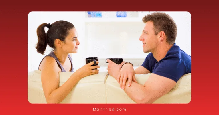 A woman and a man sit on a white couch, facing each other and holding black mugs, discussing communication strategies to reduce performance pressure in a bright, modern room.