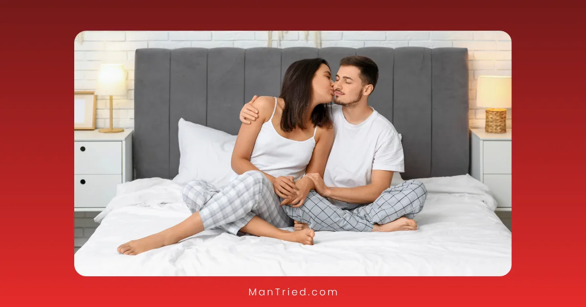 A woman kisses a man on the cheek as they sit together on a bed in matching plaid pajama pants and white shirts, with soft lighting and a cozy bedroom—highlighting intimacy supported by culturally competent sexual health providers.