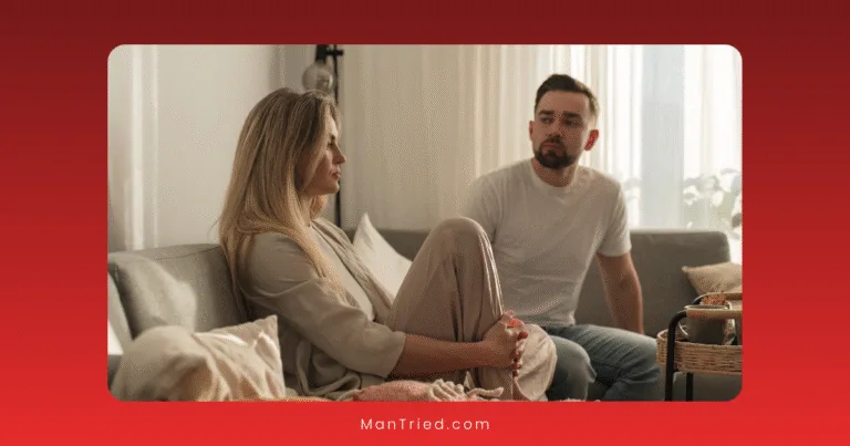 A woman and a man sit on a couch in a softly lit room, engaged in how to talk about sexual problems. The woman has her knees up and looks thoughtful, while the man listens attentively.