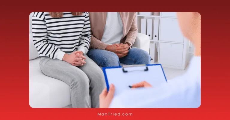 A couple sits side by side on a couch with their hands clasped, facing a counselor holding a clipboard in a bright office—illustrating the supportive environment of hybrid sexual health care.