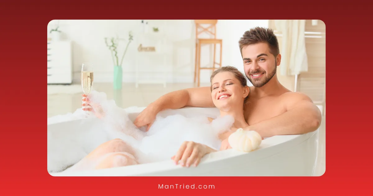 A smiling couple relaxes in a bubble bath together, enjoying each other's company. The woman holds a glass of champagne, and both look happy and content—highlighting the benefits of positive male sexual health practices in a modern, softly lit bathroom.