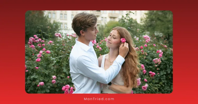 A young couple stands in a rose garden; the man, radiating quiet confidence and male sexual value, gently tucks a pink rose behind the woman's ear as they gaze at each other affectionately among blooming pink roses and lush greenery.