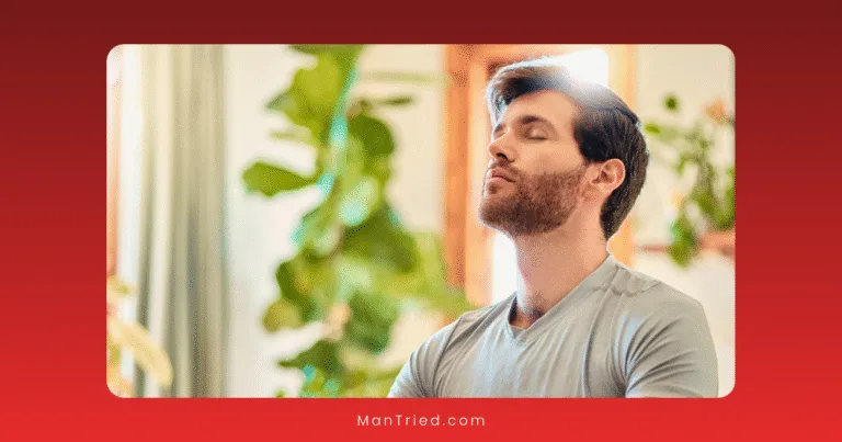 A man with a beard and short hair sits indoors with his eyes closed, embodying mindfulness for men. Green plants and soft natural light surround him.